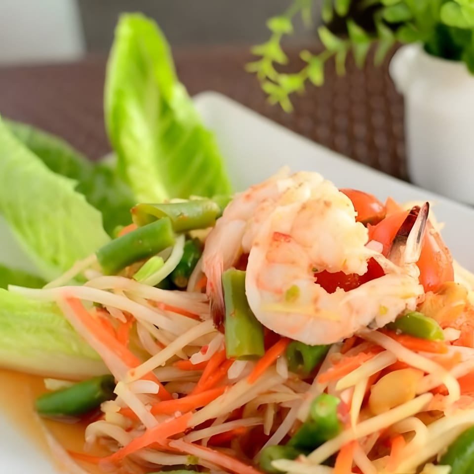 Close-up of a vibrant Thai papaya salad with shrimp, green beans, and carrots.