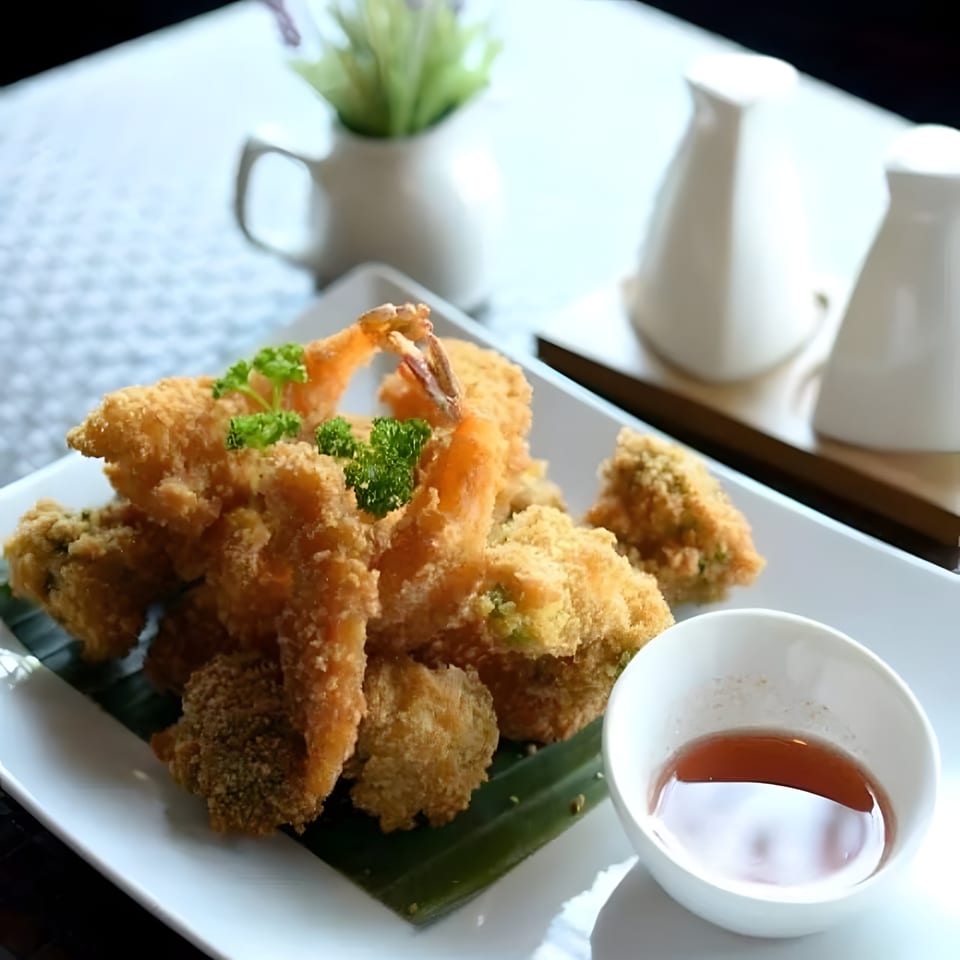 Crispy fried shrimp and vegetables on a white plate with a small bowl of dipping sauce.