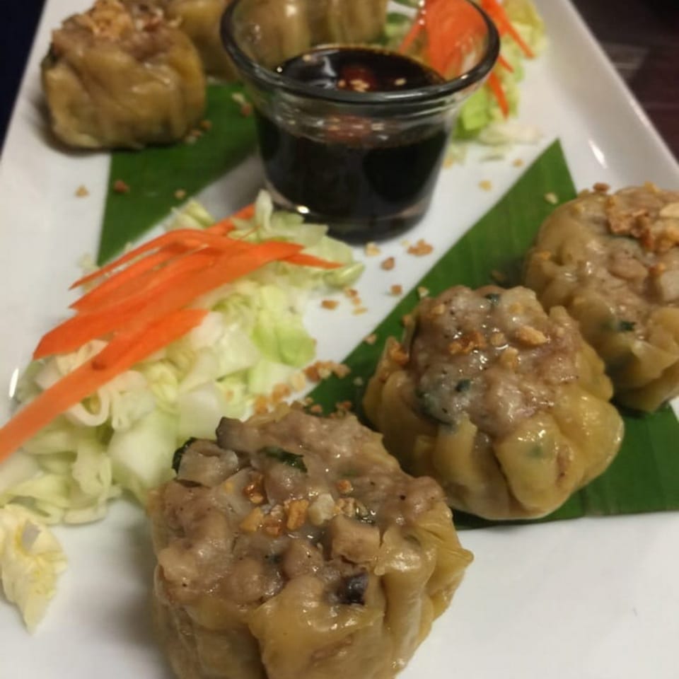 Thai dumplings with sauce and garnish on a white plate at Table Thai Bar & Bistro.
