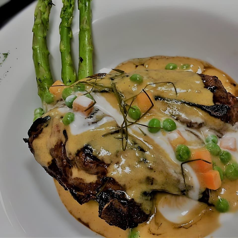 Thai dish with meat, yellow curry sauce, peas, carrots, and asparagus spears on a white plate.