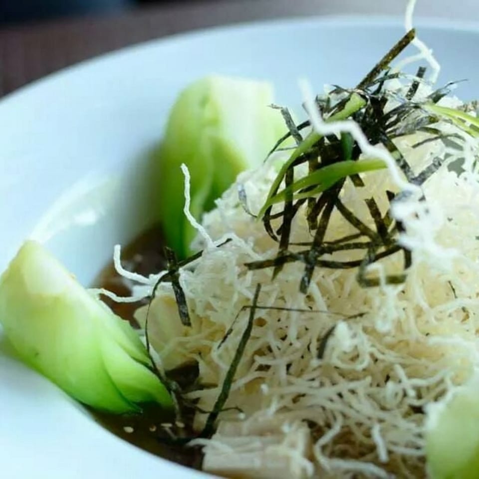 A Thai dish with white noodles, green bok choy, and dark seaweed in a white bowl.