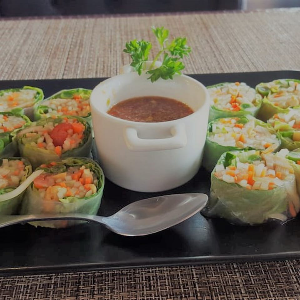 Table Thai Bar & Bistro's fresh spring rolls with dipping sauce and a spoon on a black platter.
