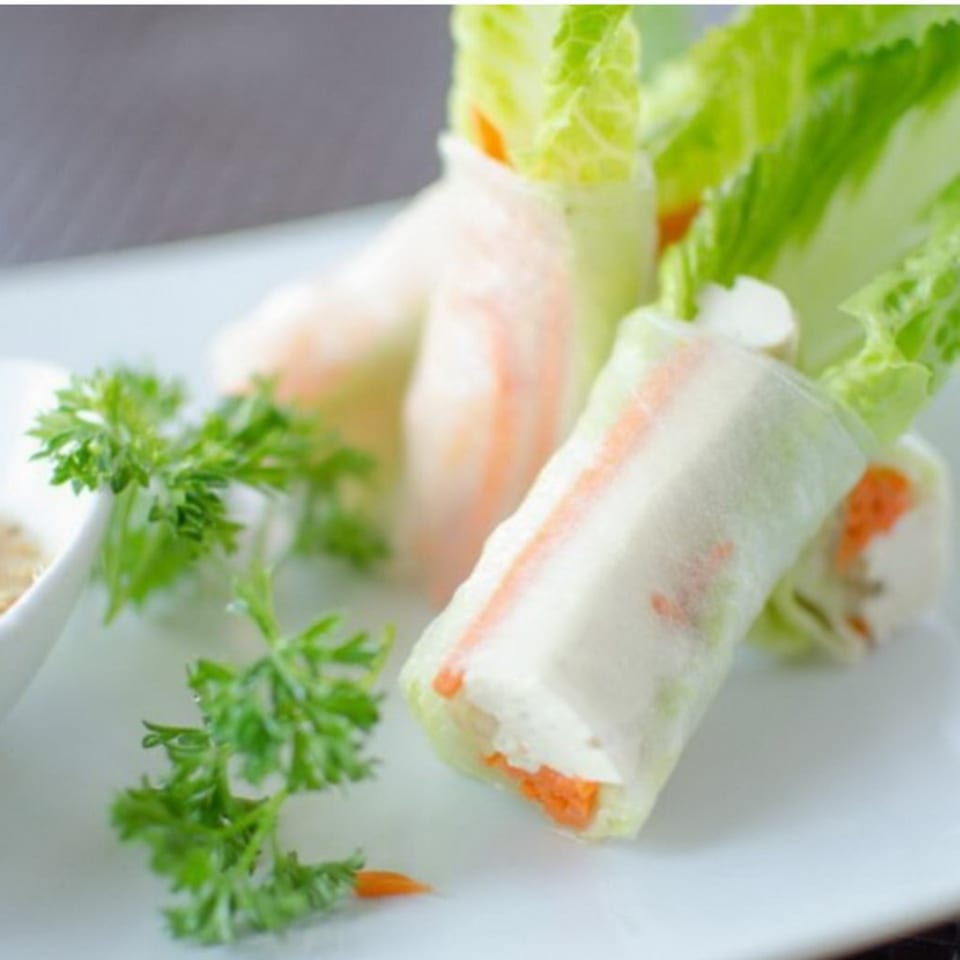 Fresh Thai spring rolls with carrots and lettuce, garnished with parsley on a white plate.