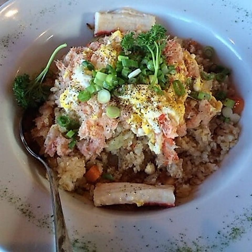 Crab fried rice with scrambled egg, green onions, and parsley in a white bowl with a spoon.