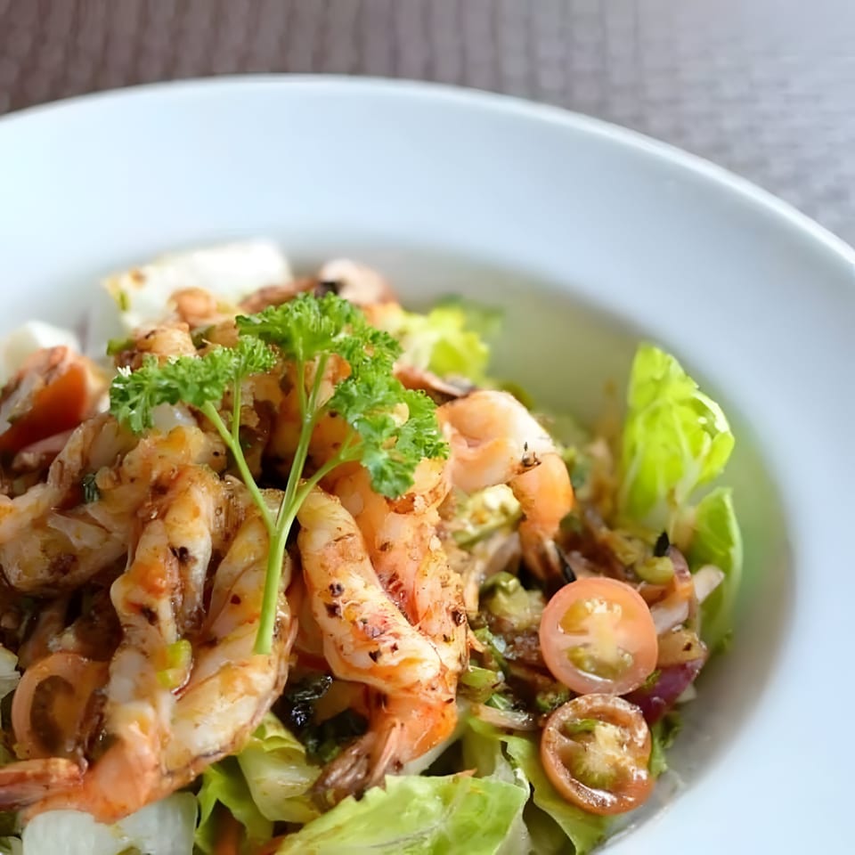 Close-up of a Thai shrimp salad with lettuce, cherry tomatoes, and parsley in a white bowl.