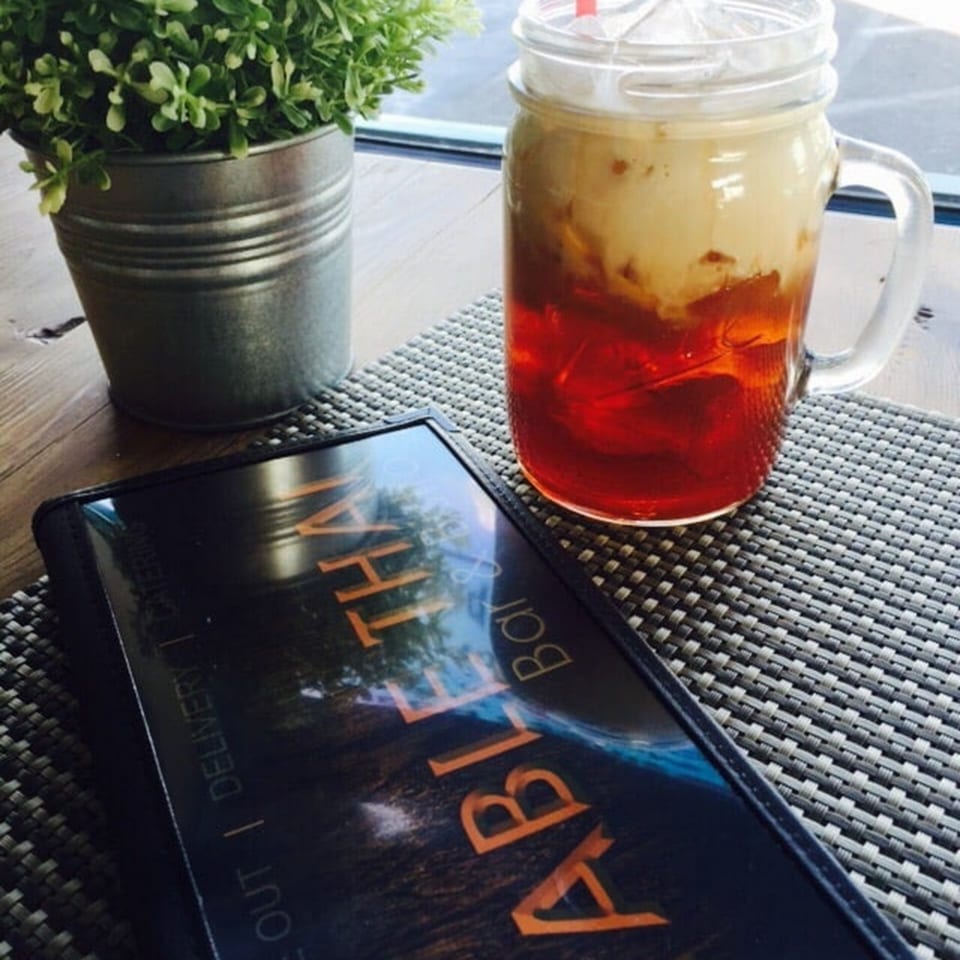 Thai iced tea in a mason jar next to a menu and potted plant on a table.