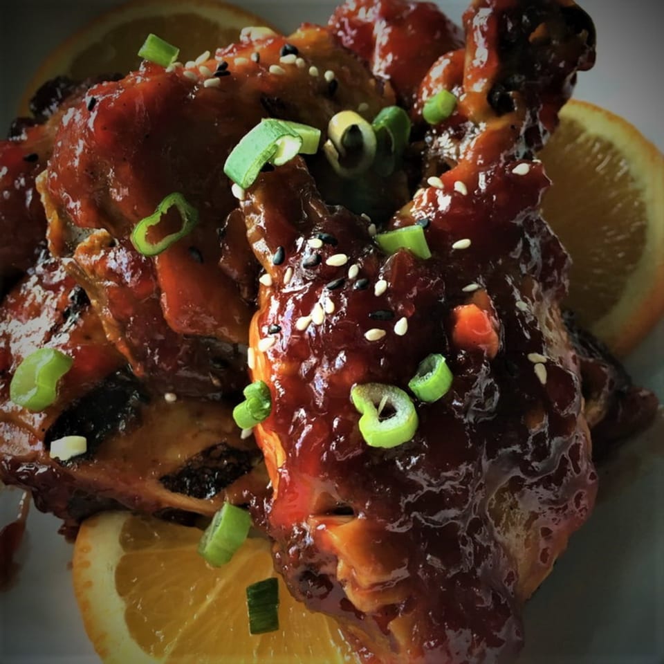 Close-up of Table Thai Bar & Bistro's sticky chicken wings, garnished with scallions, sesame seeds, and orange slices.