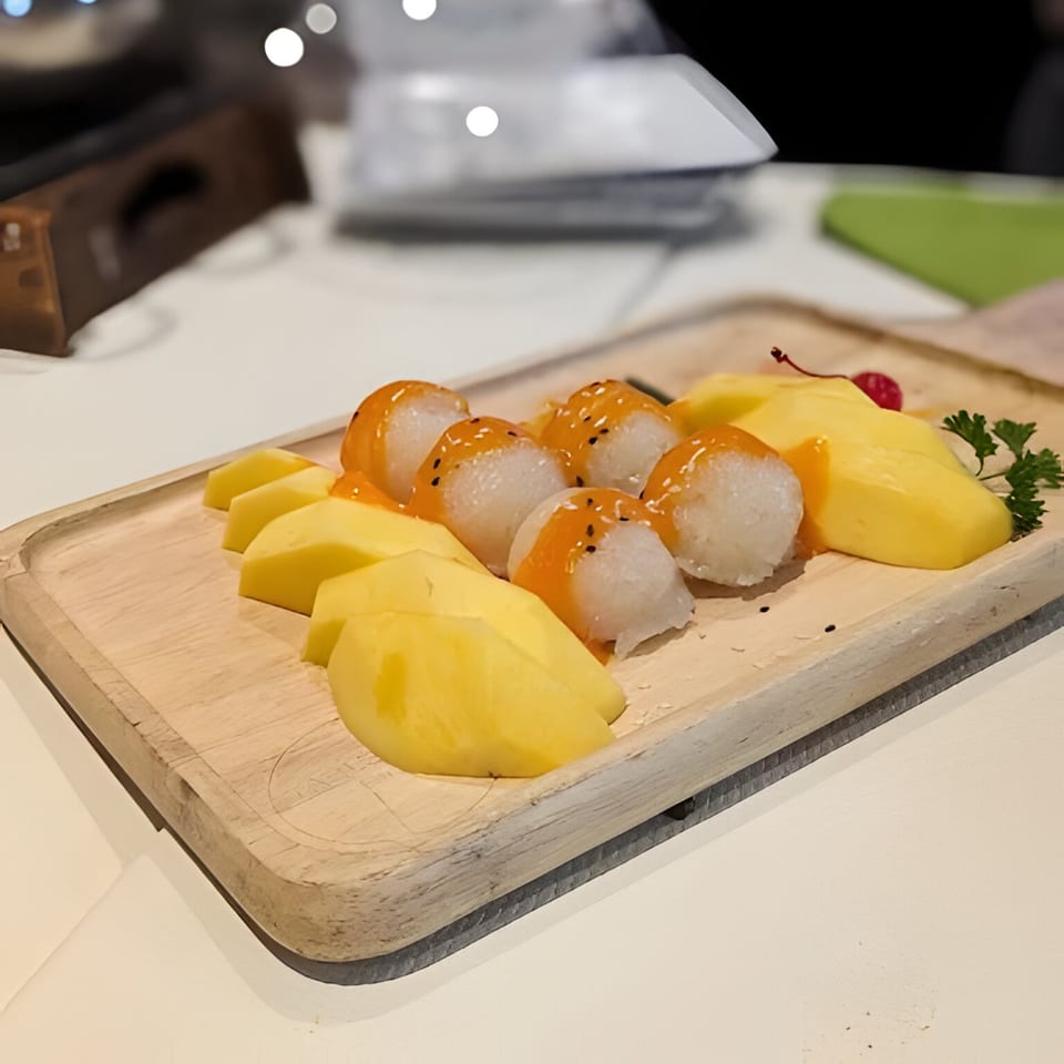 Mango sticky rice dessert with fresh mango slices, sticky rice balls, and a cherry on a wooden board.