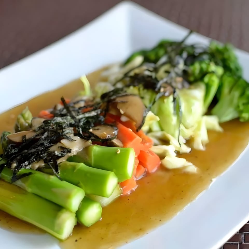 Steamed vegetables including asparagus, carrots, and broccoli, topped with seaweed and mushrooms in a sauce.