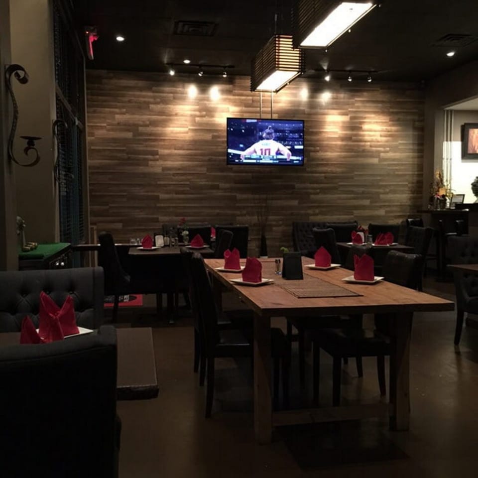 Table Thai Bar & Bistro's dimly lit dining room with wooden tables, black chairs, and red napkins.