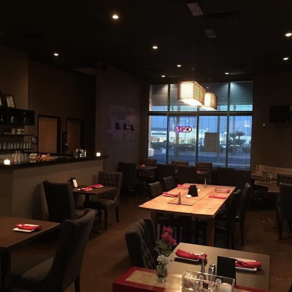Dimly lit dining room at Table Thai Bar & Bistro with tables set and an "OPEN" sign in the window.